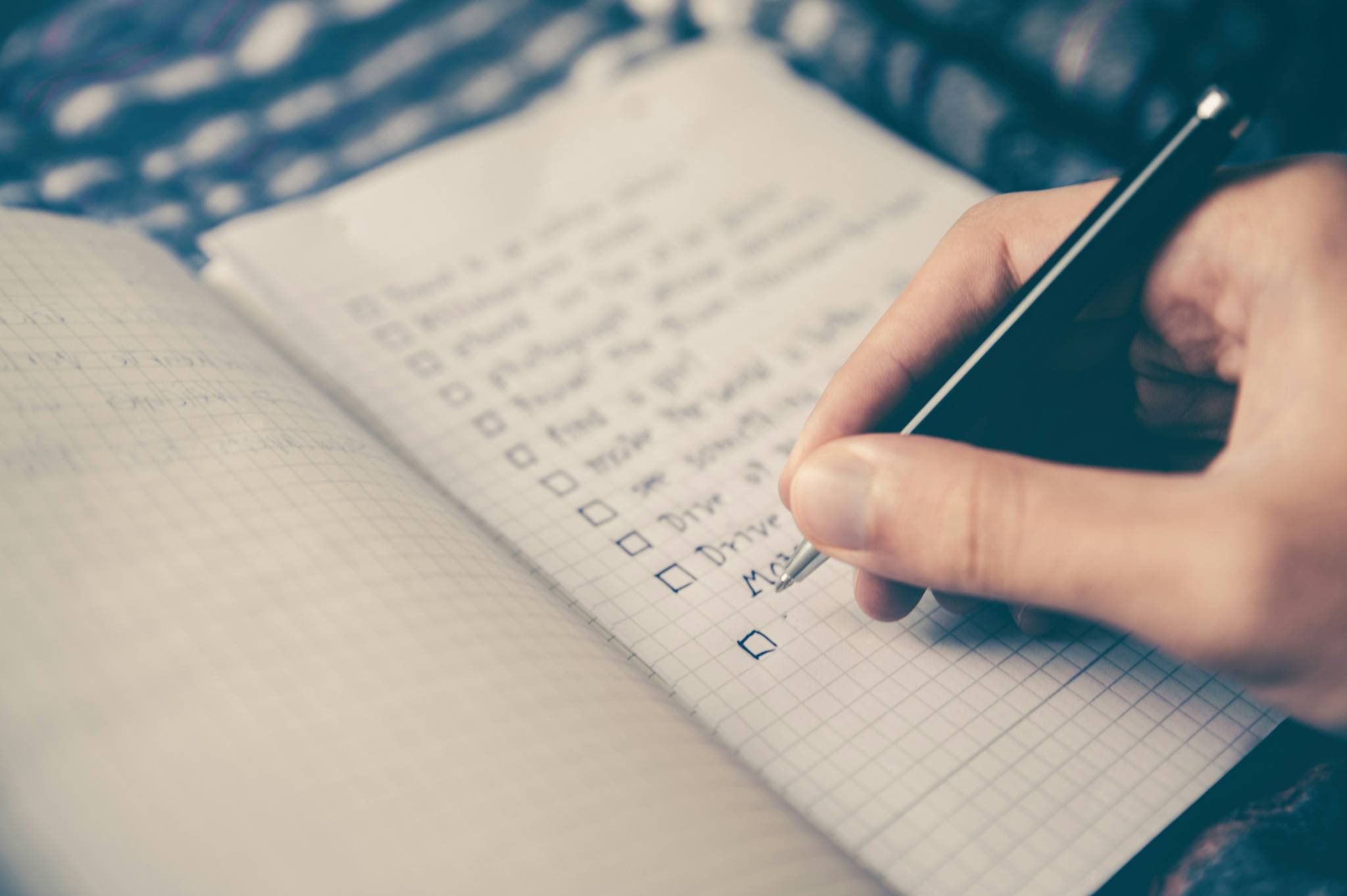 Close-up of a person writing a checklist in a grid notebook, with tasks being checked off, symbolizing organization and goal-setting.