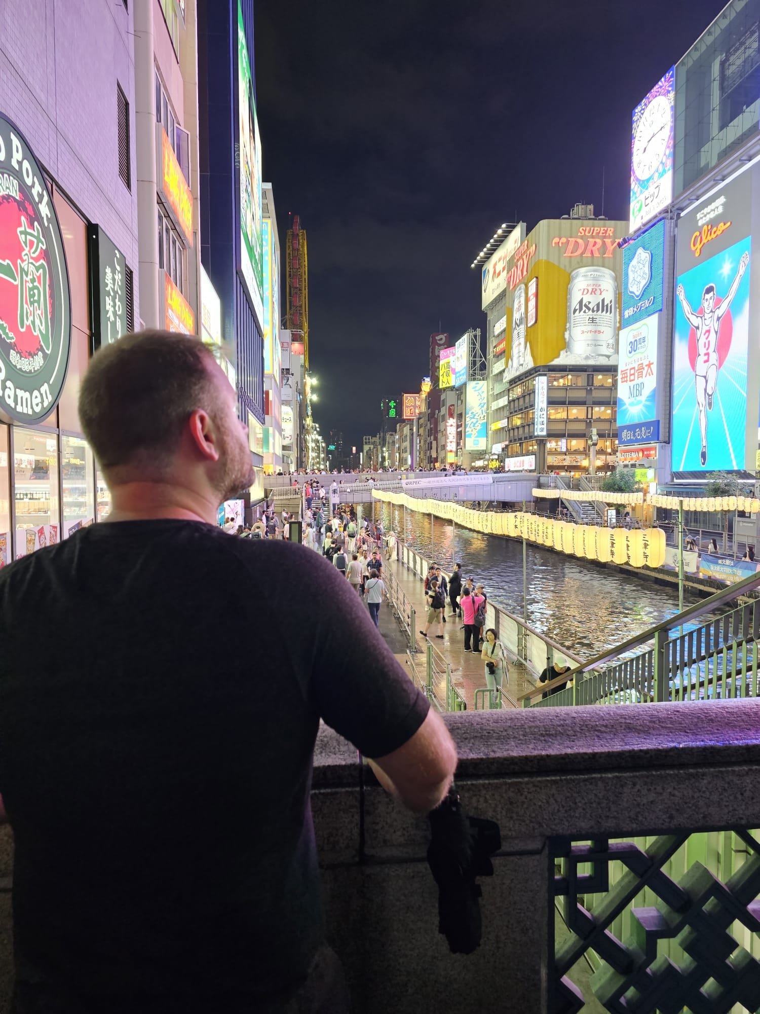 person overlooking the japanese skyline and the lights in the evening. The streets are clean and the bridge is lit up.