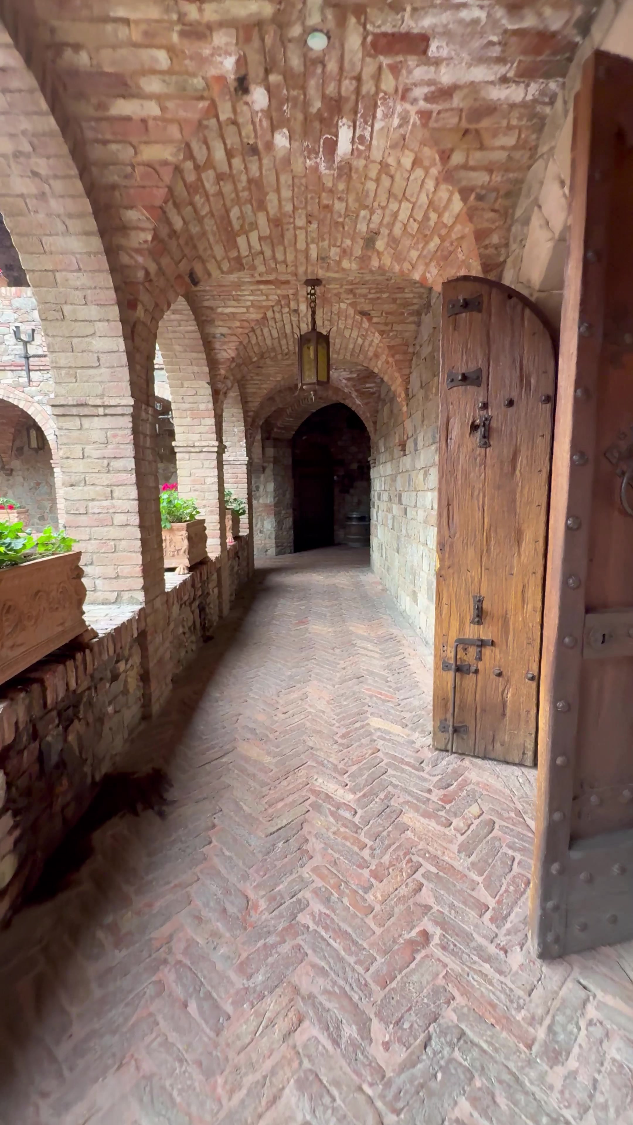 A brick-vaulted loggia corridor with lanterns and flower boxes at Castello di Amorosa