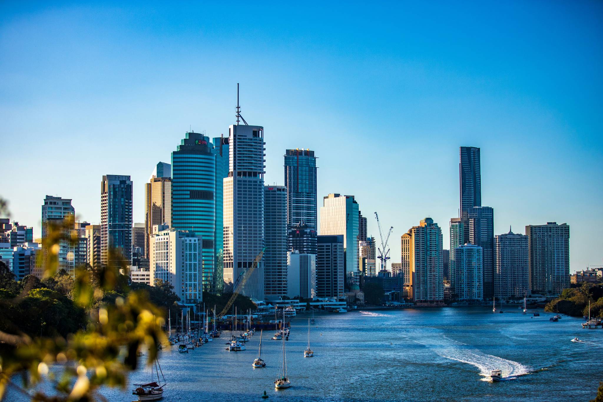 Brisbane skyline with towering modern skyscrapers along the river, with yachts floating on the calm water during a clear day, an ideal scene to explore during a working holiday Brisbane.