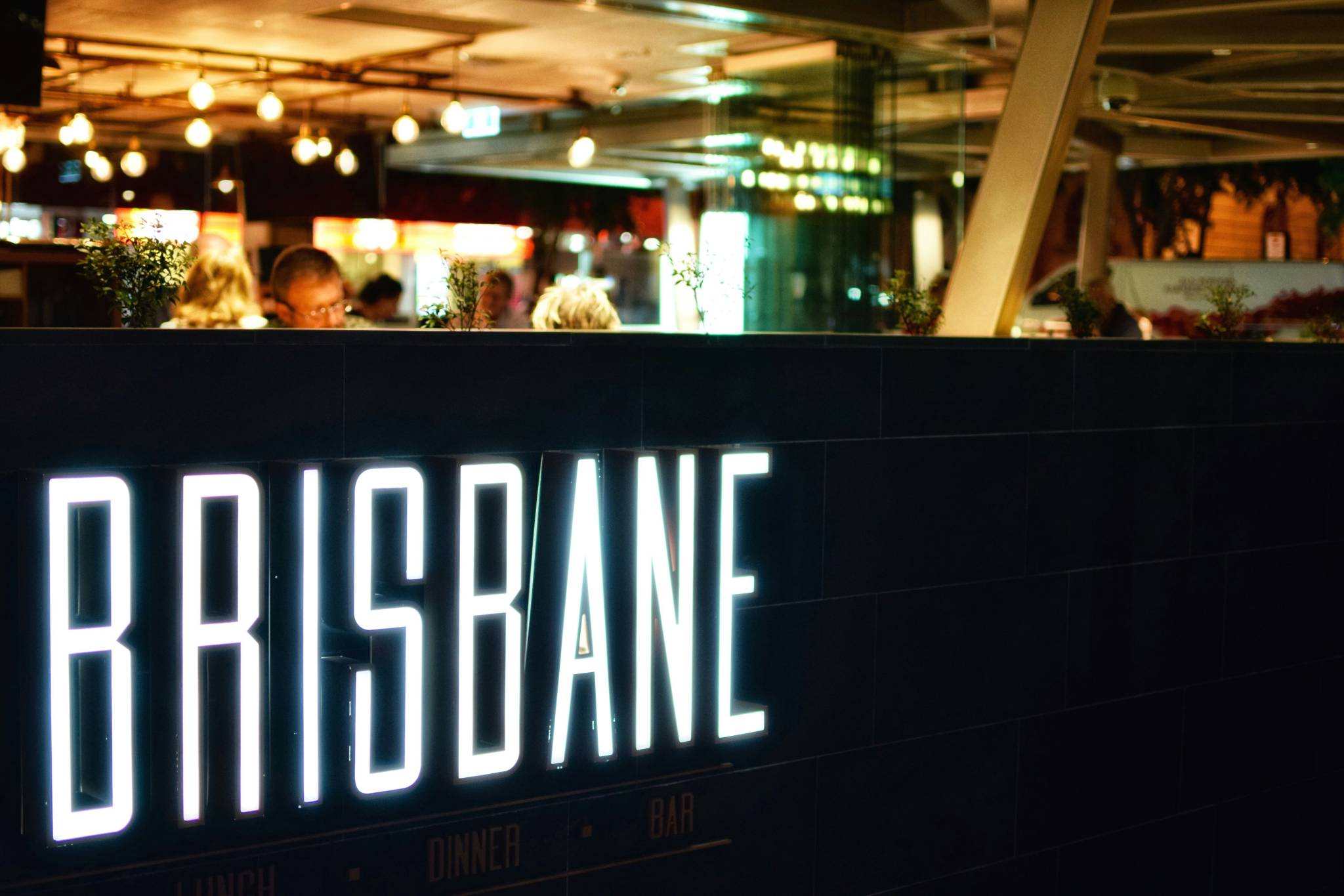 Close-up of a neon 'Brisbane' sign in a vibrant restaurant setting, emphasizing the lively dining scene to experience on a Brisbane working holiday.