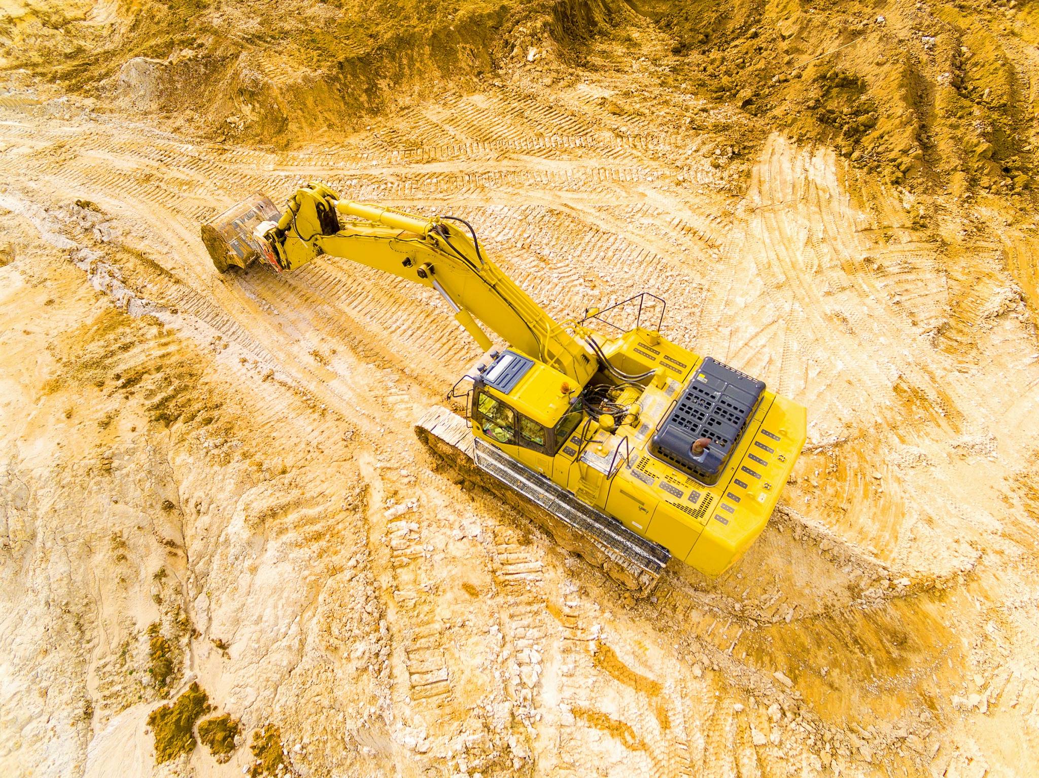 A large yellow excavator digging at a mining site, with tire tracks visible on the sandy ground. This machine is commonly used in FIFO jobs, making it ideal for workers on a working holiday.