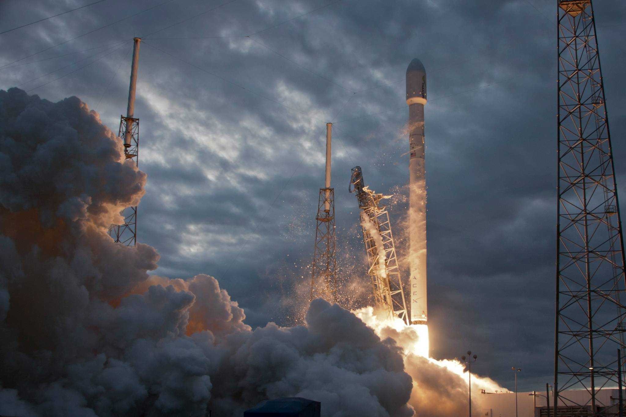 A rocket launching into the sky from a space discovery center, leaving a trail of smoke and flames as it ascends. The bright plume contrasts with the blue sky, symbolizing exploration and technological advancement.