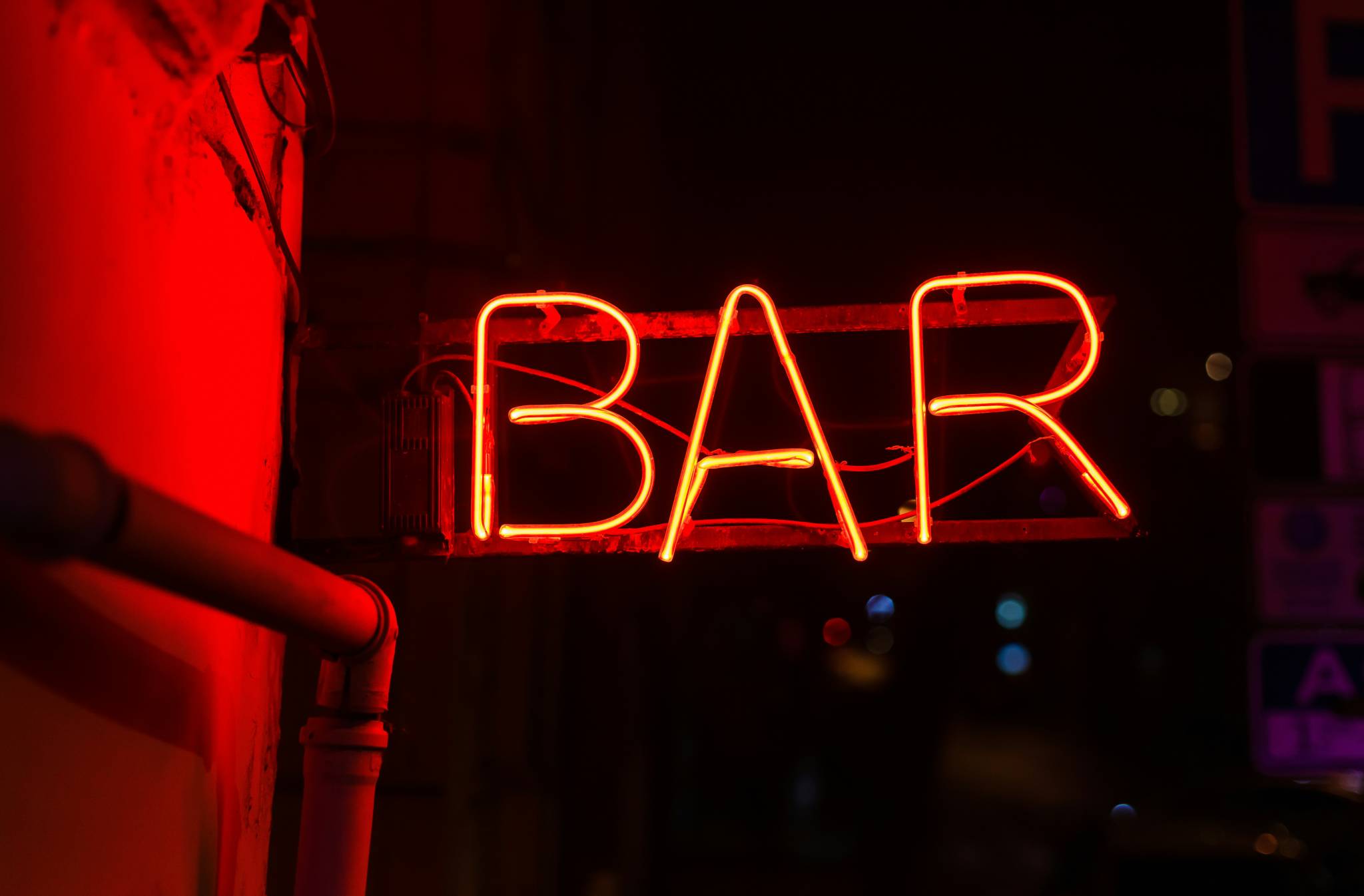 A glowing red neon sign reading "BAR" on a dimly lit wall. The bright, inviting sign is typical of the vibrant nightlife around the best backpacker bars in Sydney.