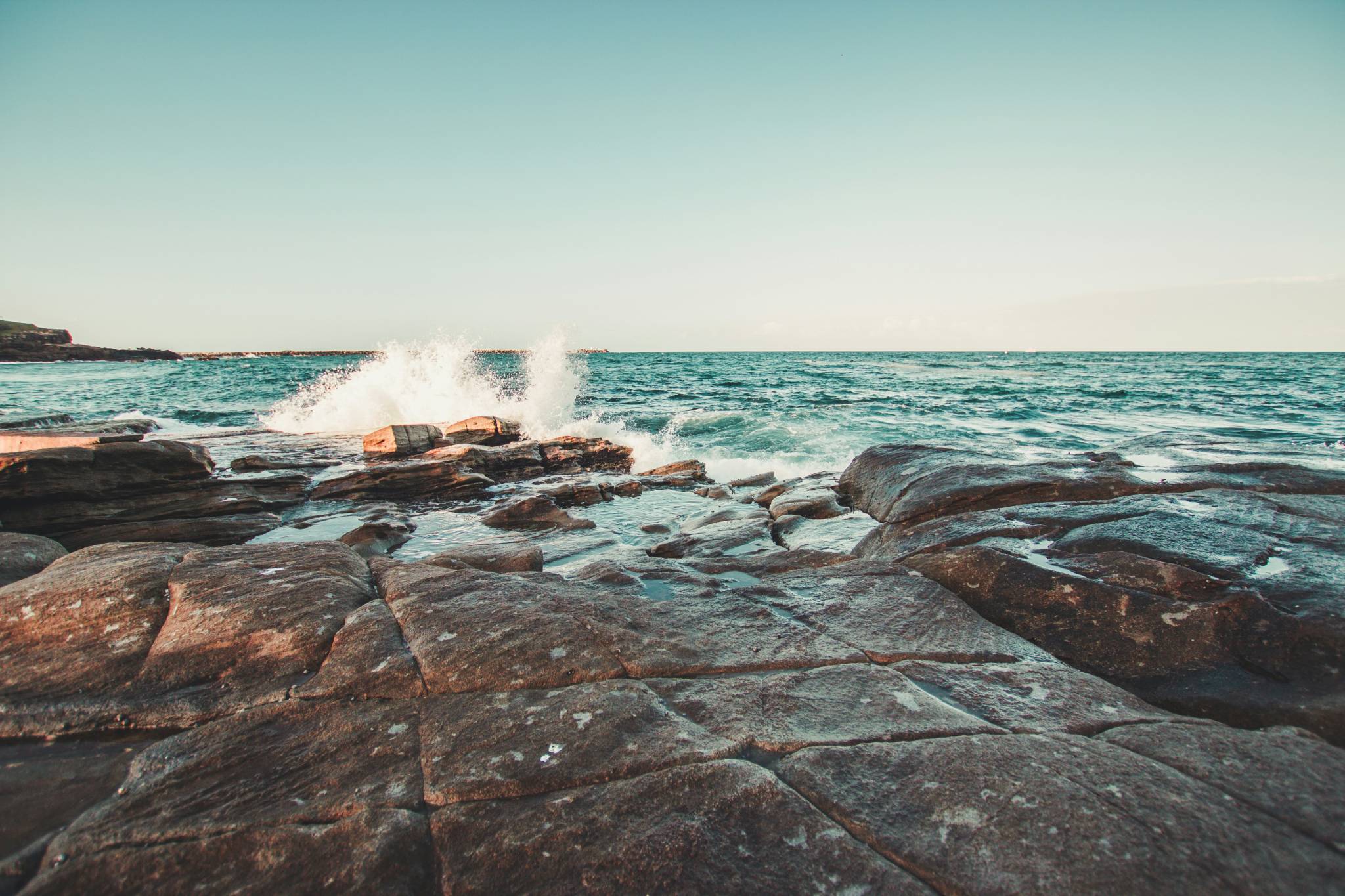 Waves crashing on the rocky shore in Yamba, NSW, with ocean water splashing against the stones under a clear sky. Exploring the rocky coastline is one of the best things to do in Yamba NSW for those who love scenic views and ocean vibes.