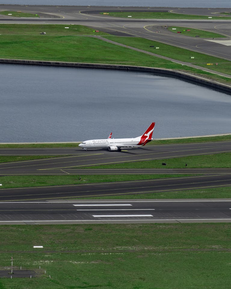 A commercial airplane on the runway against a backdrop of green fields and water.