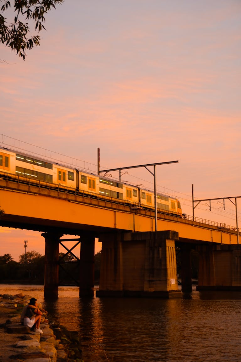 A picturesque train crosses a bridge over water in Sydney at sunset, radiating a warm glow.