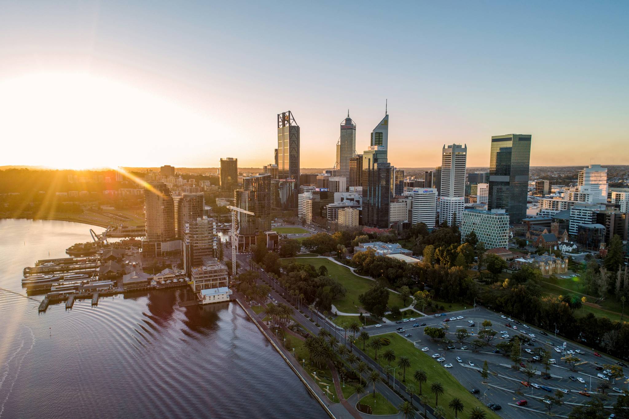 An aerial view of Perth's central business district at sunrise, with high-rise buildings, the Swan River, and green parks, capturing the perfect balance of work and leisure for a working holiday in Perth.