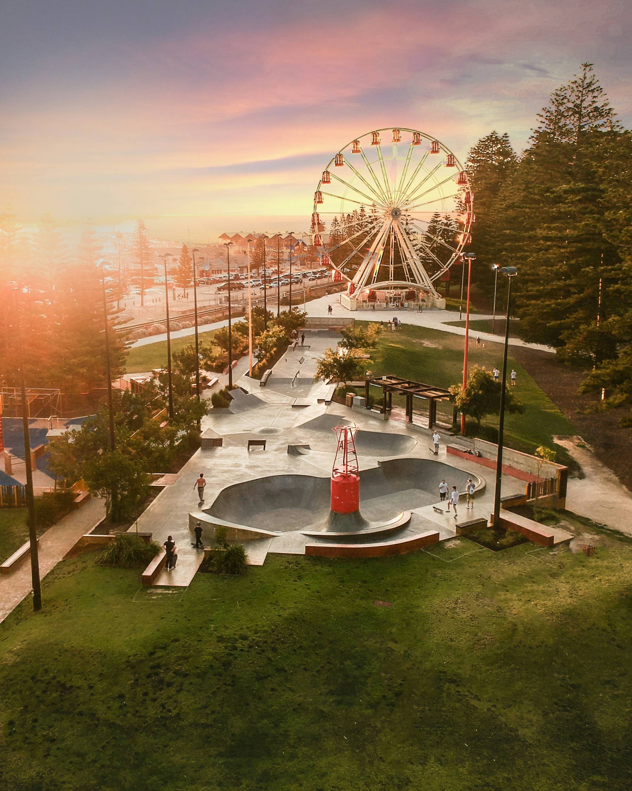 A picturesque sunset over a Ferris wheel and skatepark in Fremantle, WA, with people enjoying the outdoor space. The scene captures the coastal charm and vibrant culture of Fremantle.