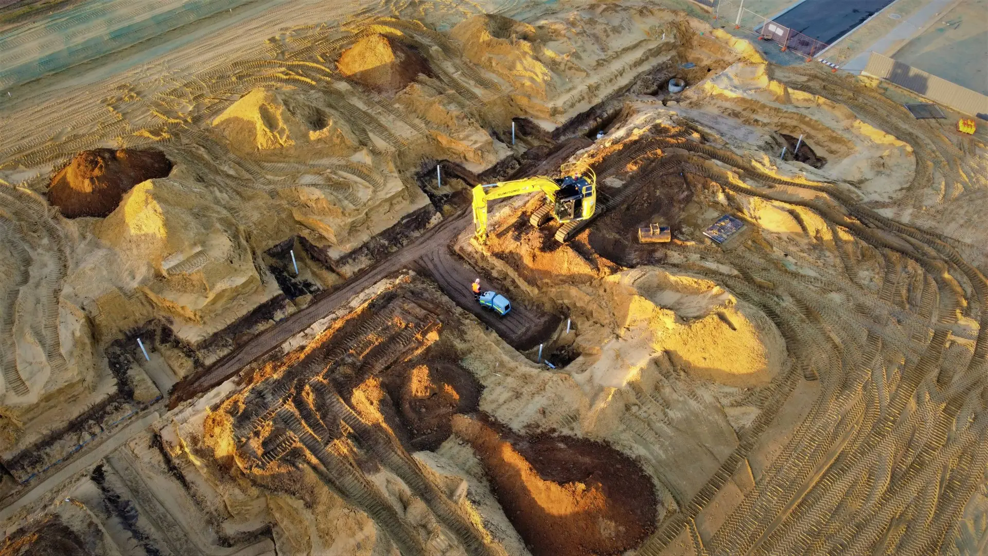 An aerial view of an excavation site with multiple mounds of dirt, a yellow excavator, and a small vehicle, likely part of a FIFO job site for those working holiday opportunities in mining or construction.