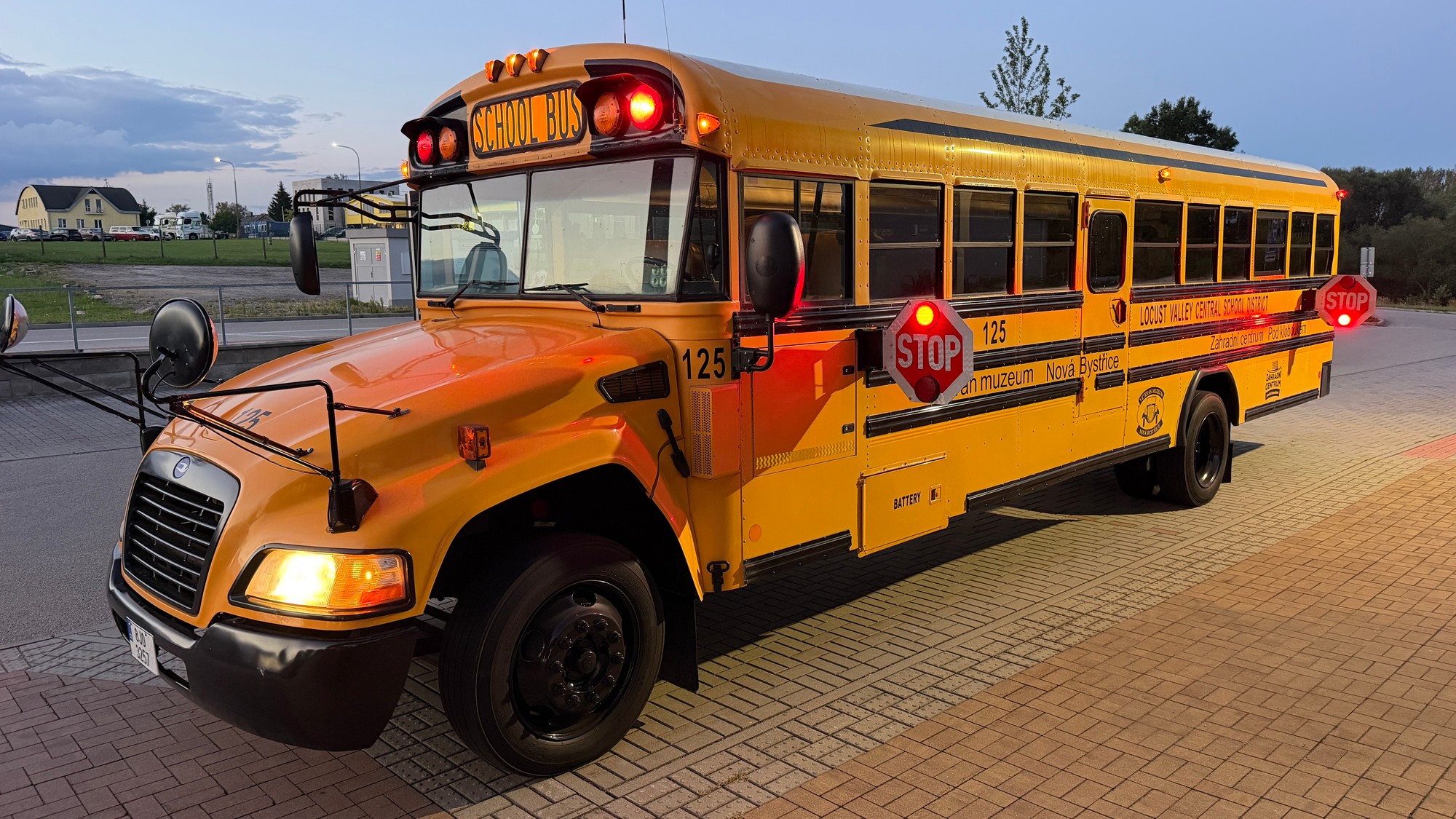 Americký žlutý školní bus za soumraku se zapnutými výstražnými světly