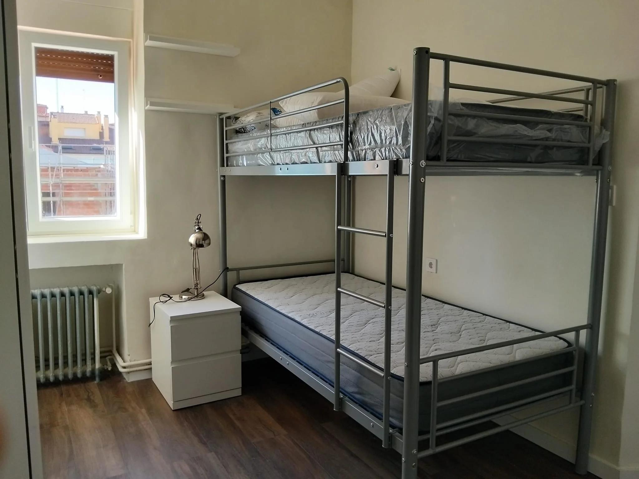 Habitación doble con litera, mesilla y ventana en el apartamento del Colegio Mayor San Juan Evangelista, Valladolid