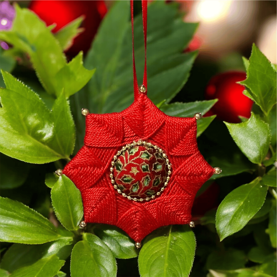 Handmade red yarn-wrapped star ornament with a gold bead frame around its festive fabric centre, hanging on red satin ribbon