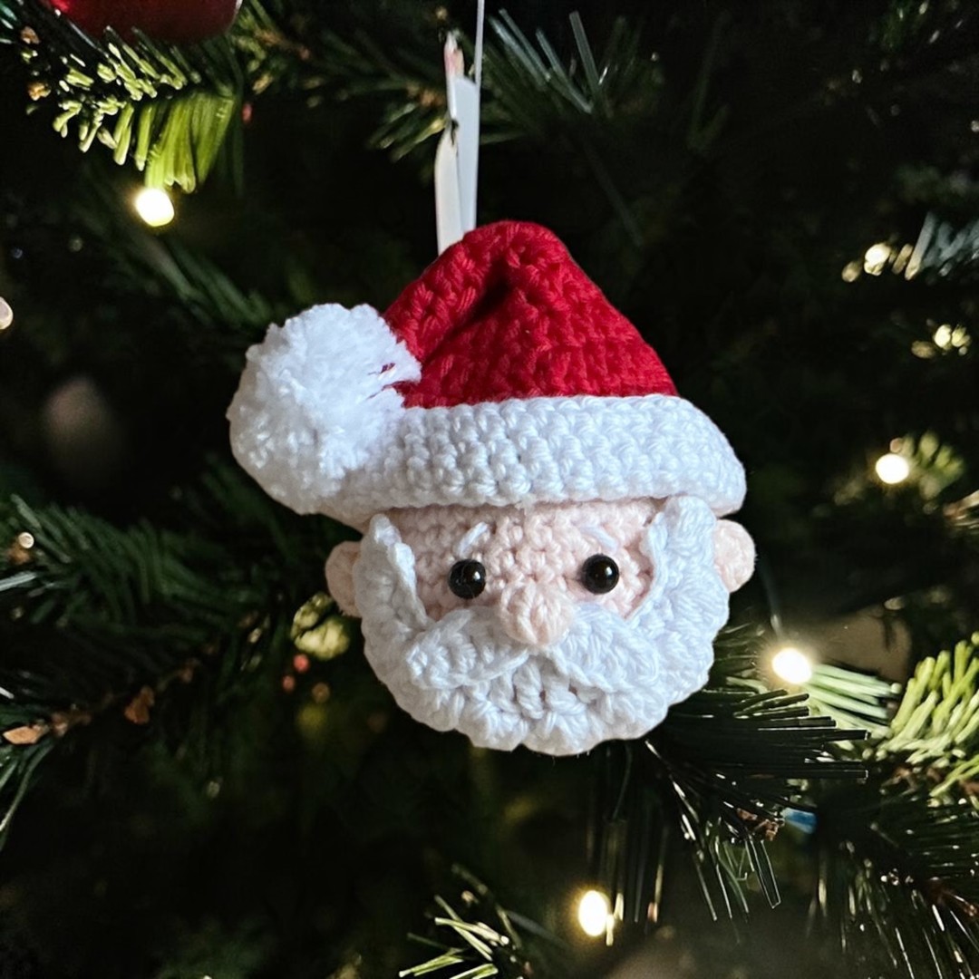 Crochet Santa face ornament photographed on the woodland floor among pine needles and leaves