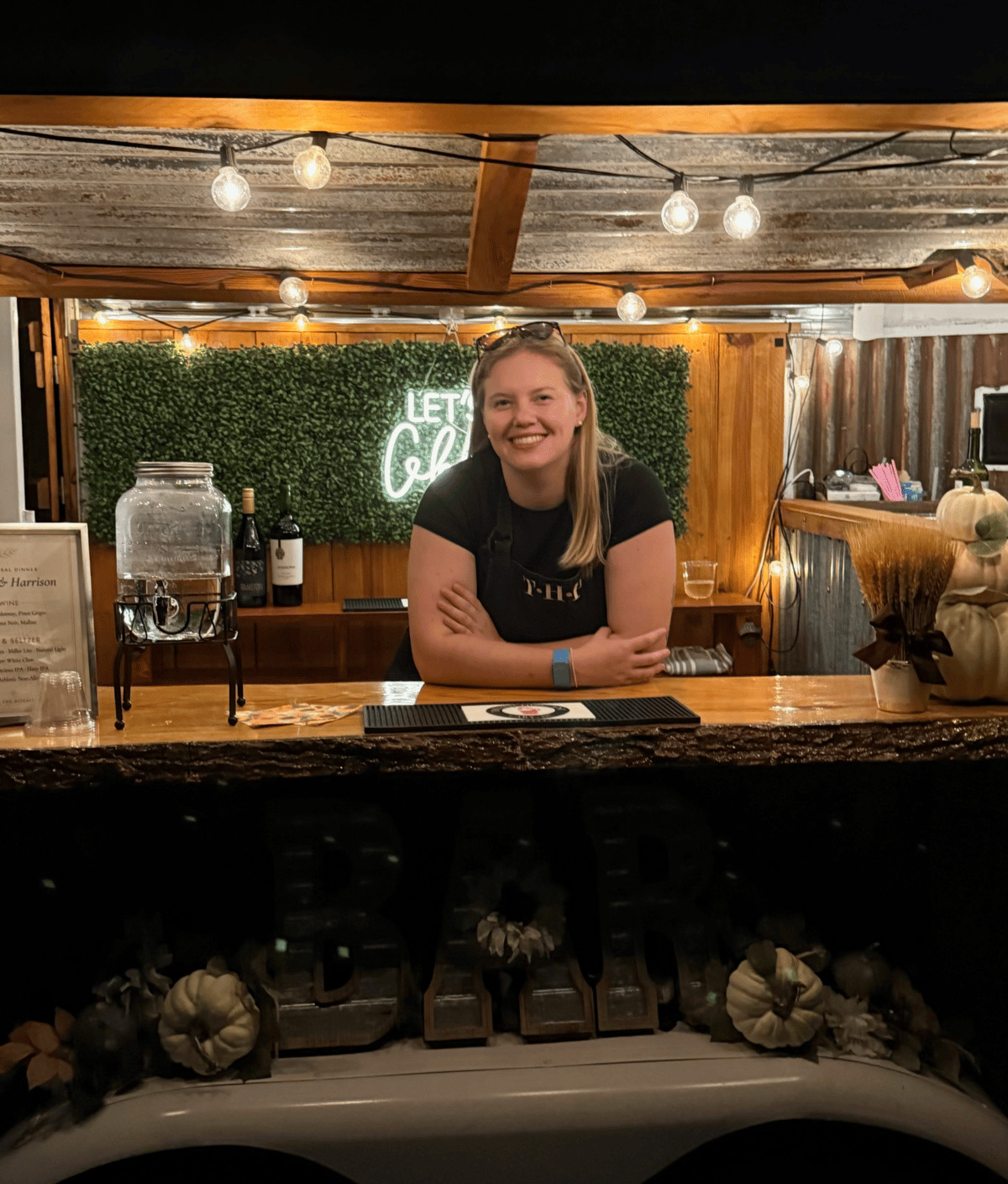 Bartender serving from the warmly lit Hitching Post bar at an evening wedding