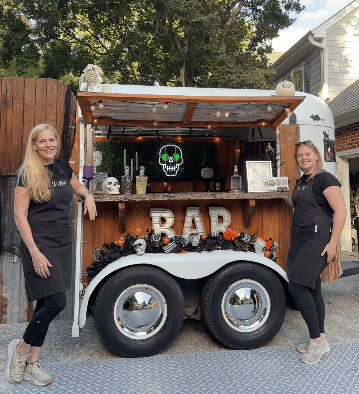 Lisa and Olivia of The Hitching Post in aprons beside the Halloween-decorated trailer