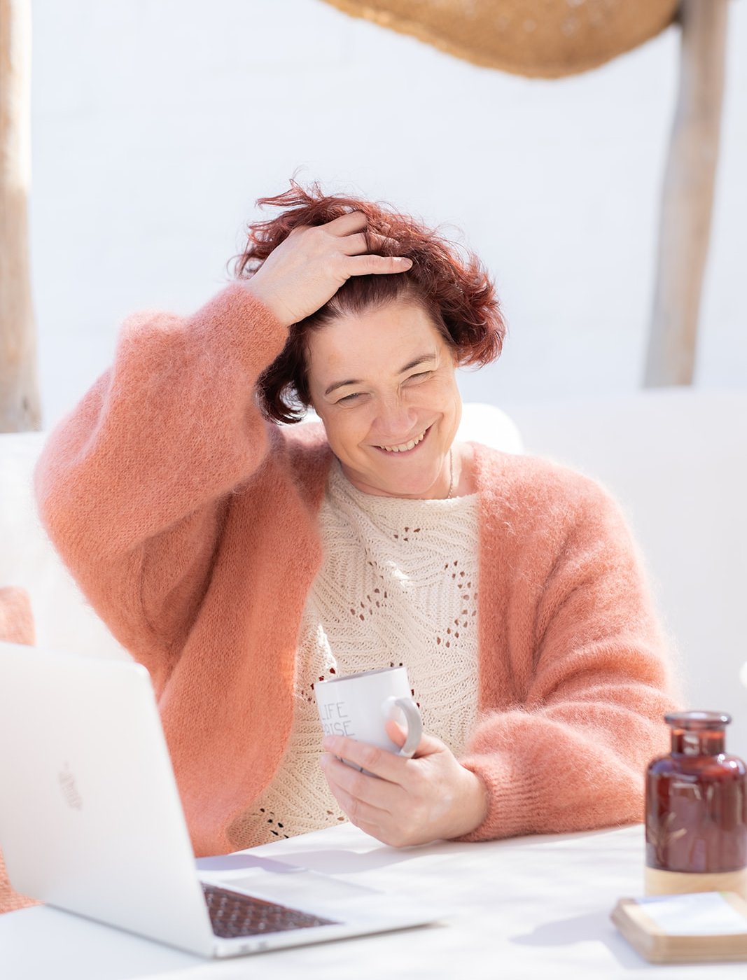 Maya Vereecken lachend aan haar bureau in haar roze trui