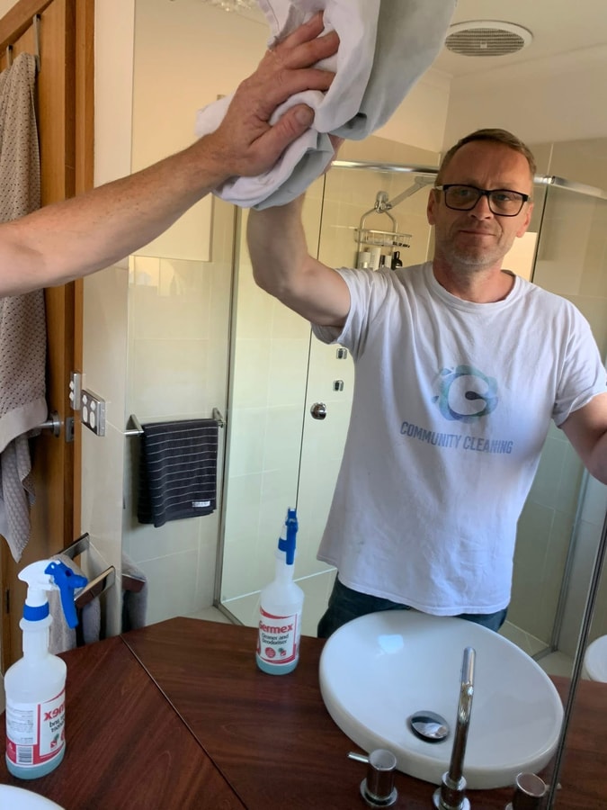 A Community Cleaning team member cleaning a bathroom mirror in South Brighton during a house clean