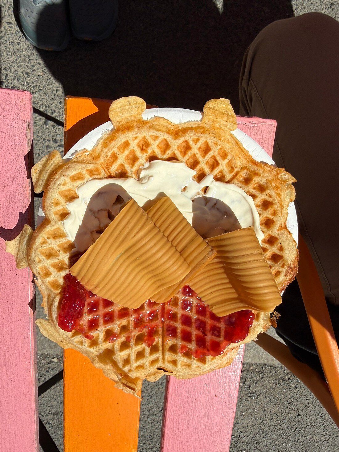 Heart-shaped Norwegian waffle with brown cheese, sour cream and raspberry jam on a pink table