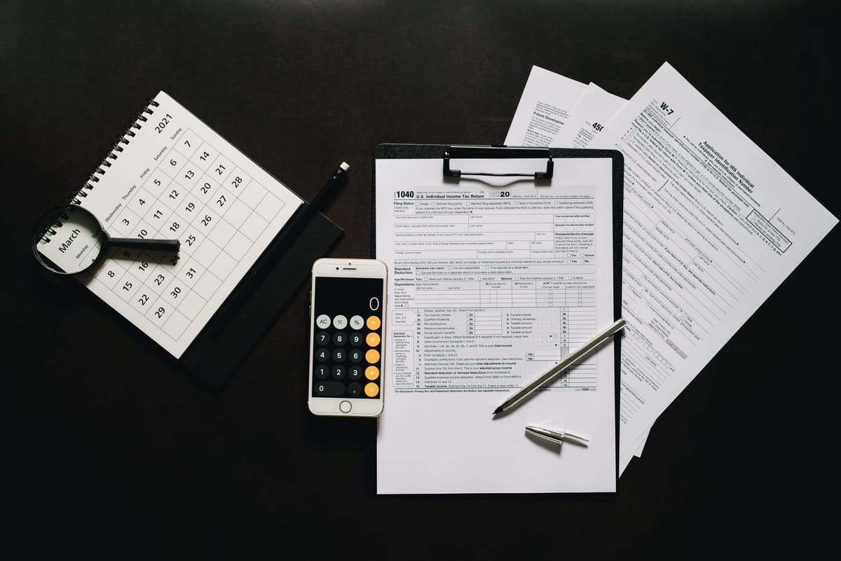 A flat lay of tax forms, a calculator, a pen and paperwork on a desk