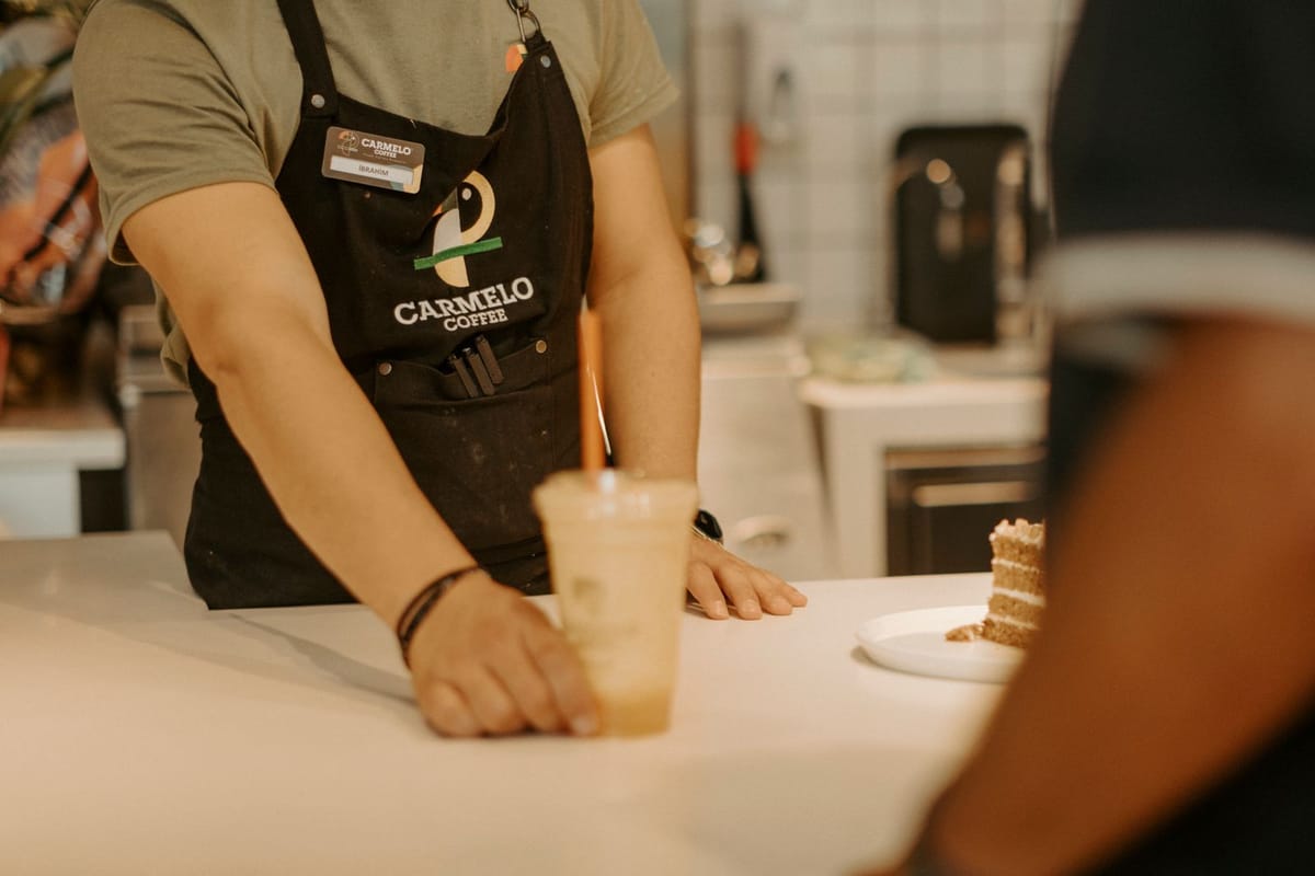 A barista in an apron serving an iced coffee across a cafe counter