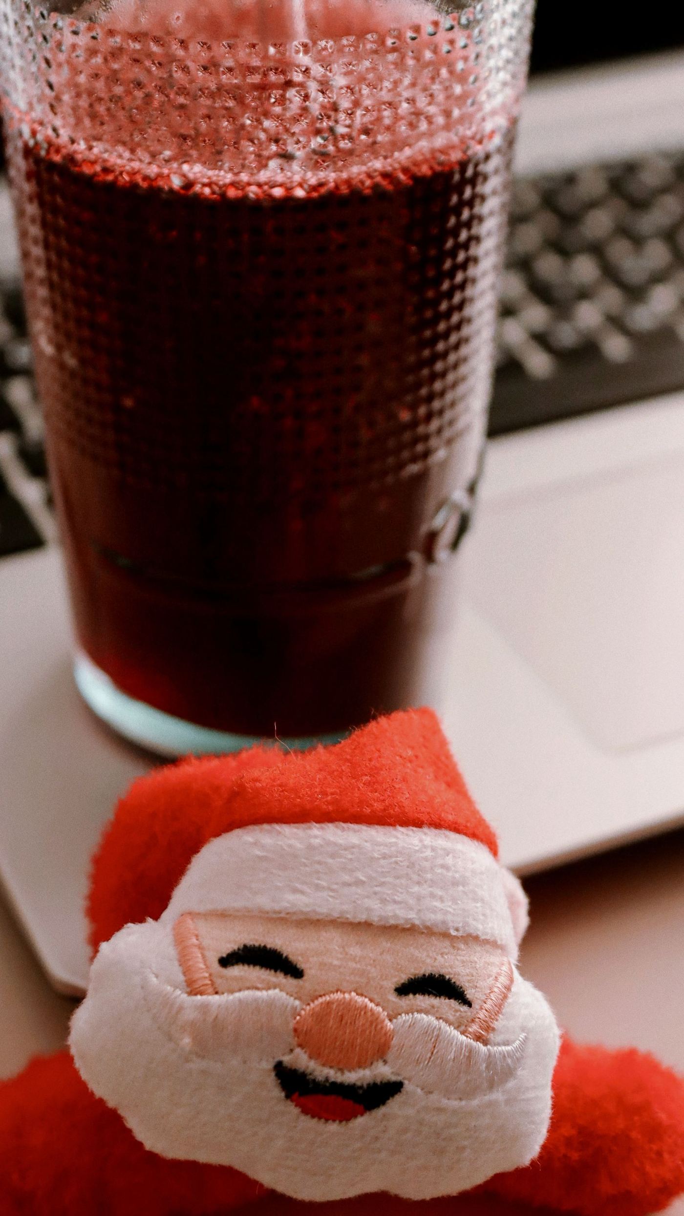 Glass of red julebrus Christmas soda fizzing beside a small smiling Santa figure