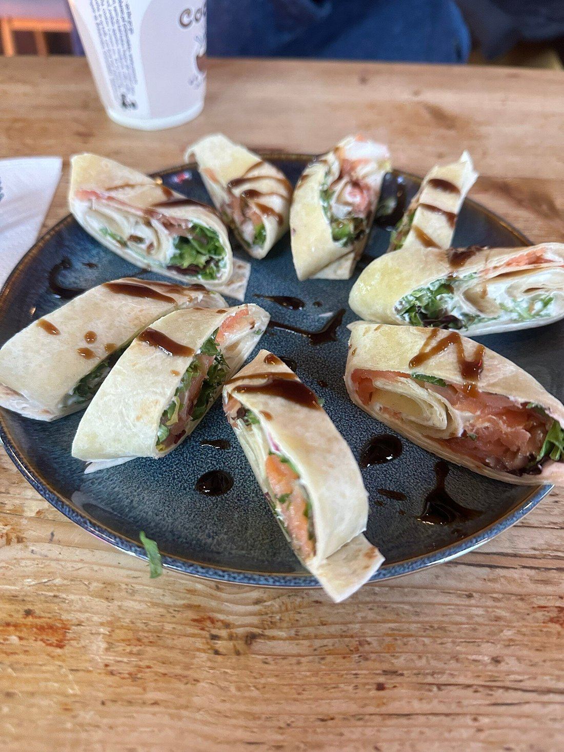 Norwegian lefse wraps filled with salmon, salad and cream, drizzled with balsamic glaze on a blue plate