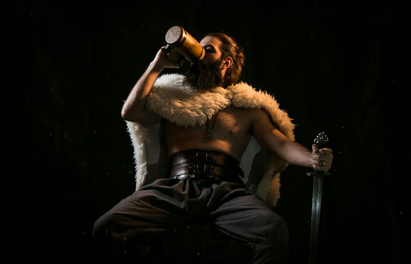 Bearded Viking in a fur cloak drinking from a wooden tankard with a sword in hand