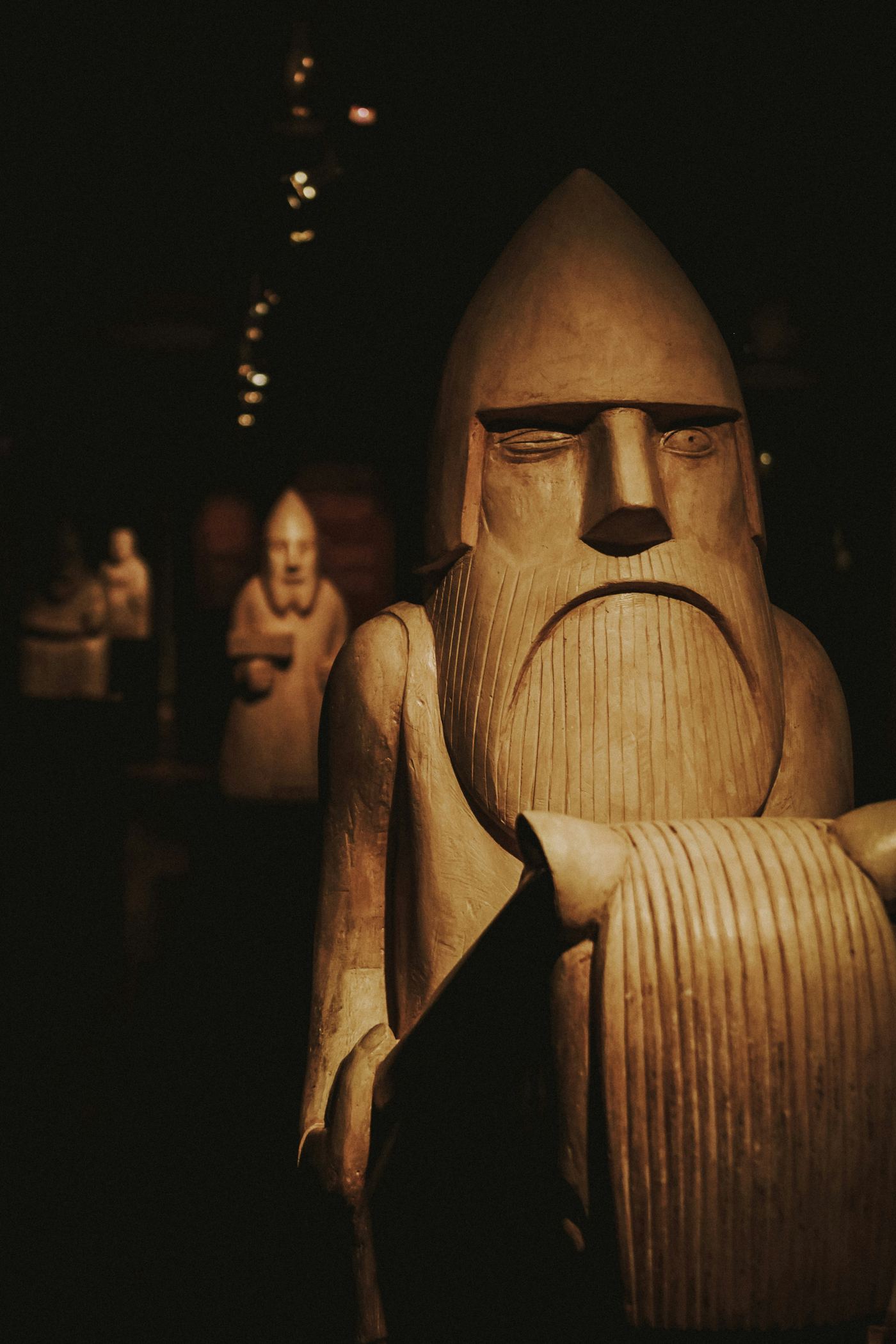 Carved wooden figure of a bearded Norse god sitting on his throne in a dimly lit museum