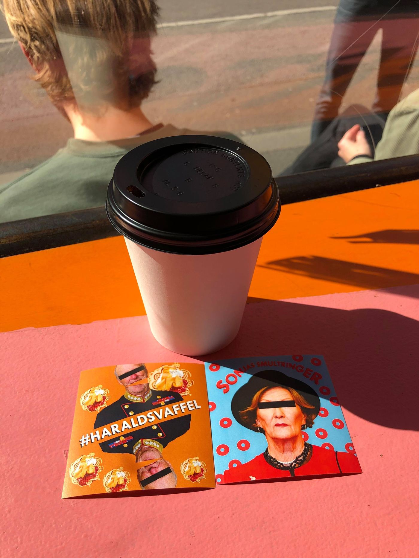 Takeaway coffee cup on a sunny windowsill next to playful stickers from a local café