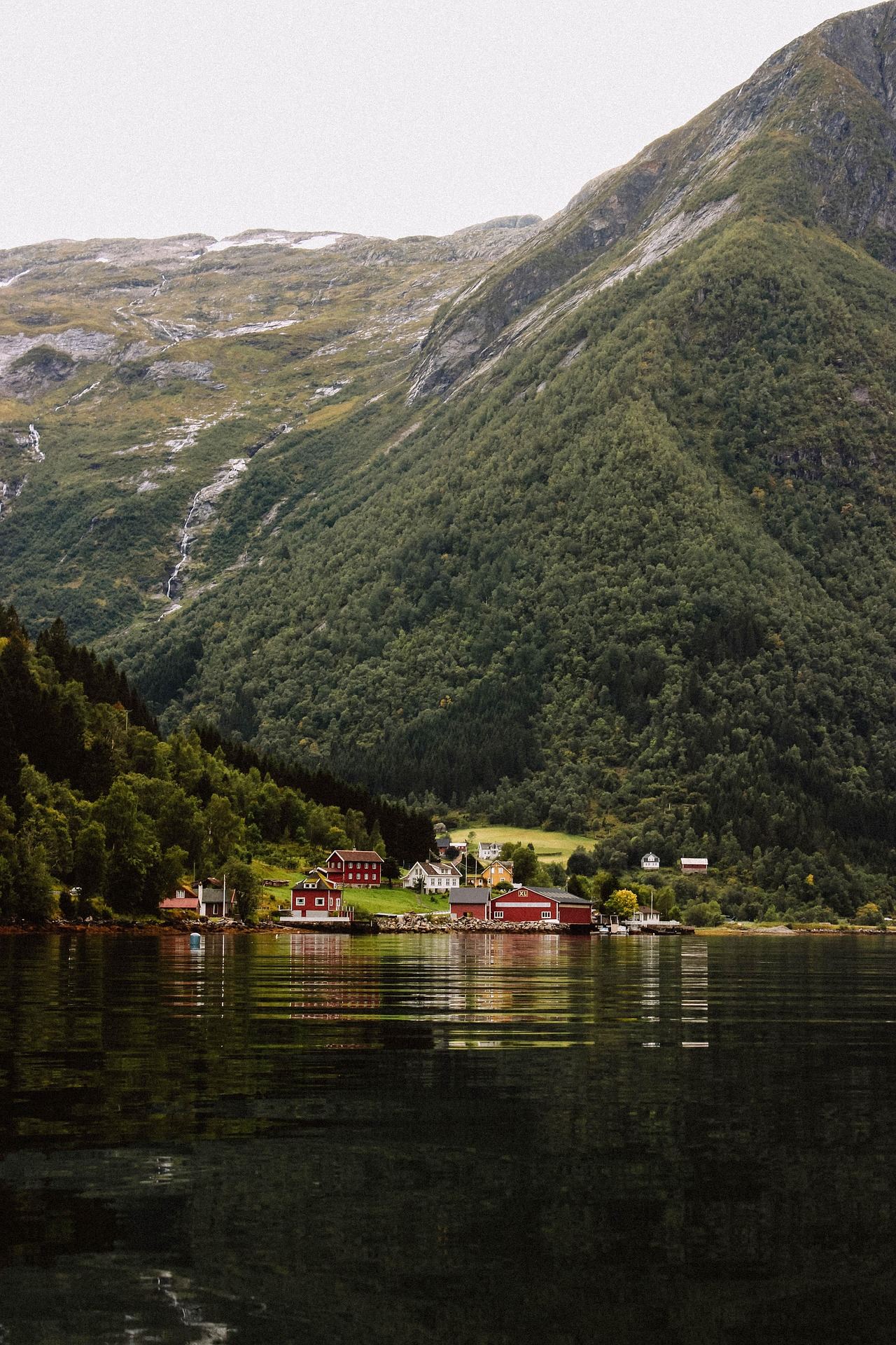 Red wooden houses by a fjord at the foot of steep green mountains in Norway