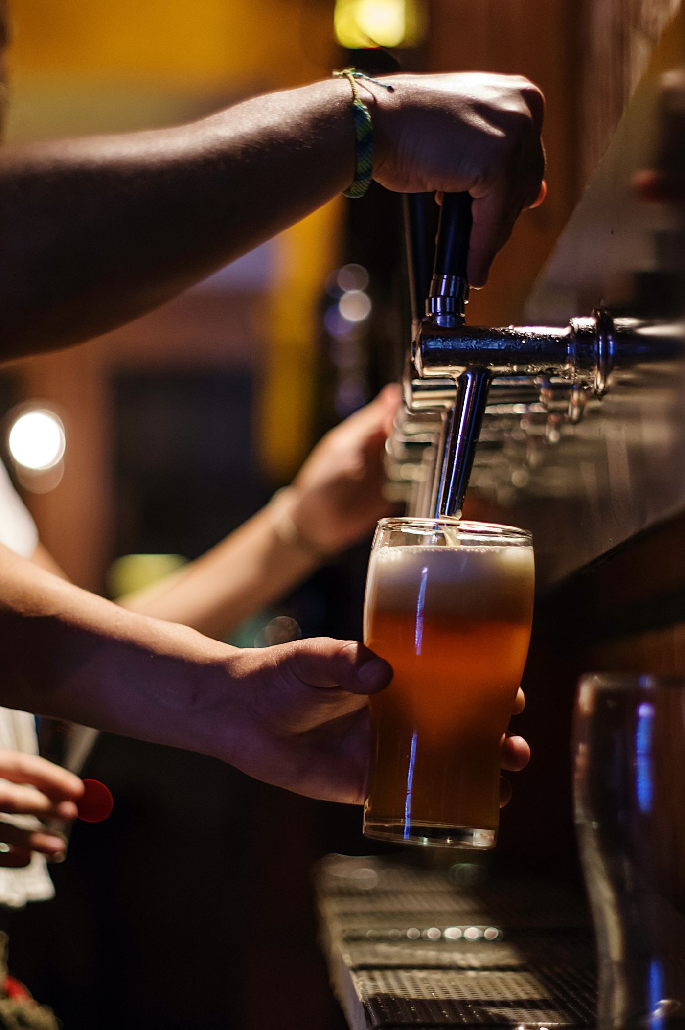 Bartender pouring an amber beer from a tap into a glass in a busy Oslo bar