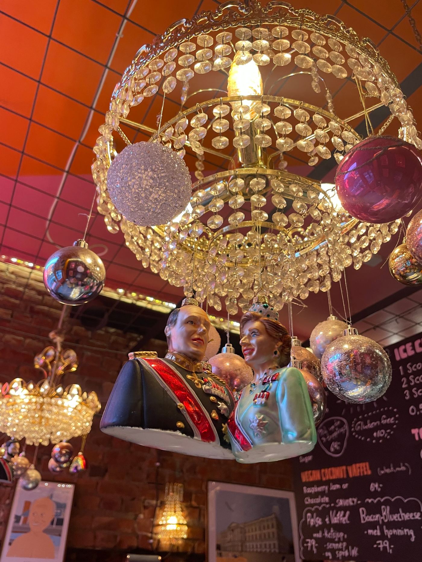 Christmas baubles, including a royal couple, hanging from a crystal chandelier in a cosy Oslo café