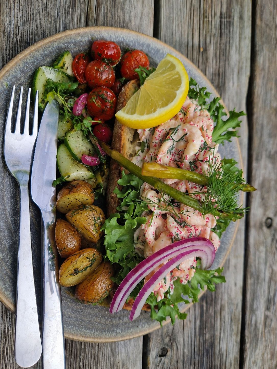 A full Norwegian dinner plate with an open shrimp sandwich, roasted tomatoes, potatoes and salad