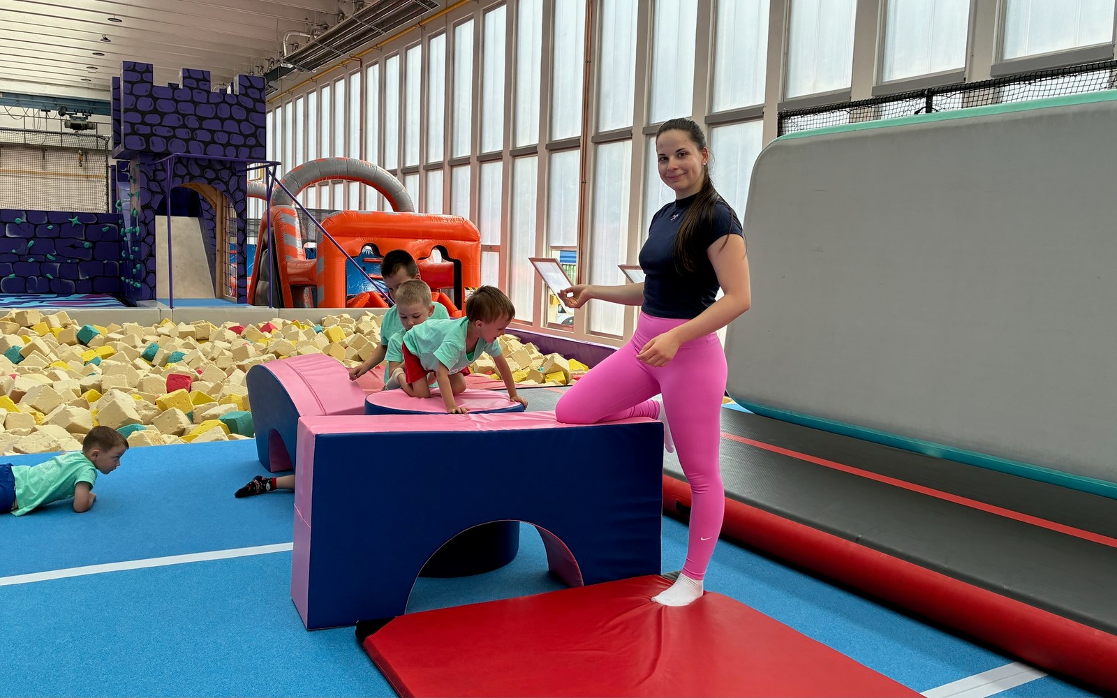 Trenérka s malými dětmi, foam pit a nafukovačky v pozadí