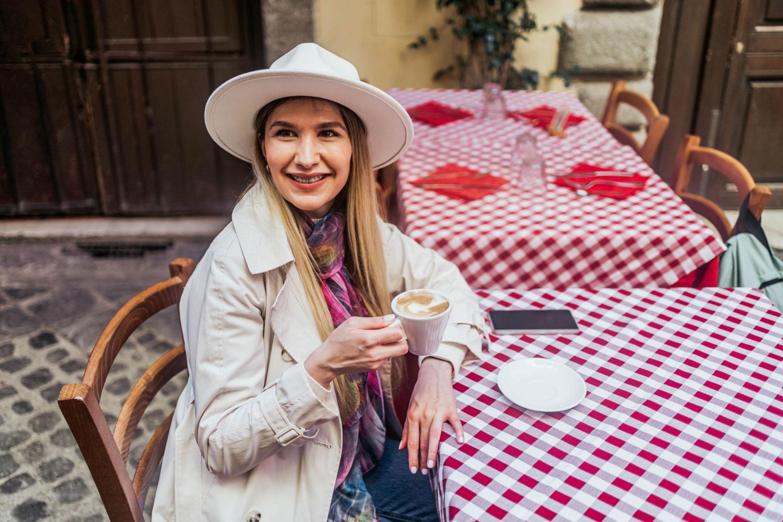 Žena v bílém klobouku s cappuccinem u stolku s červenobílou ubrusovou tyčí v italské kavárně