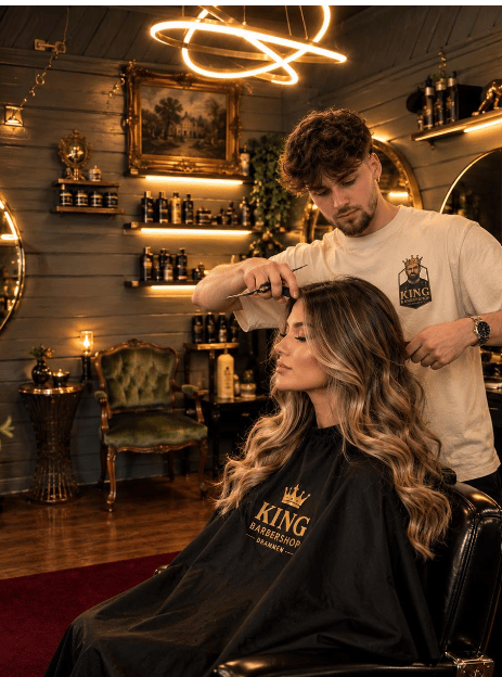 Interiøret i King Barbershop i Drammen med varm belysning, gullrammer og barberer i arbeid