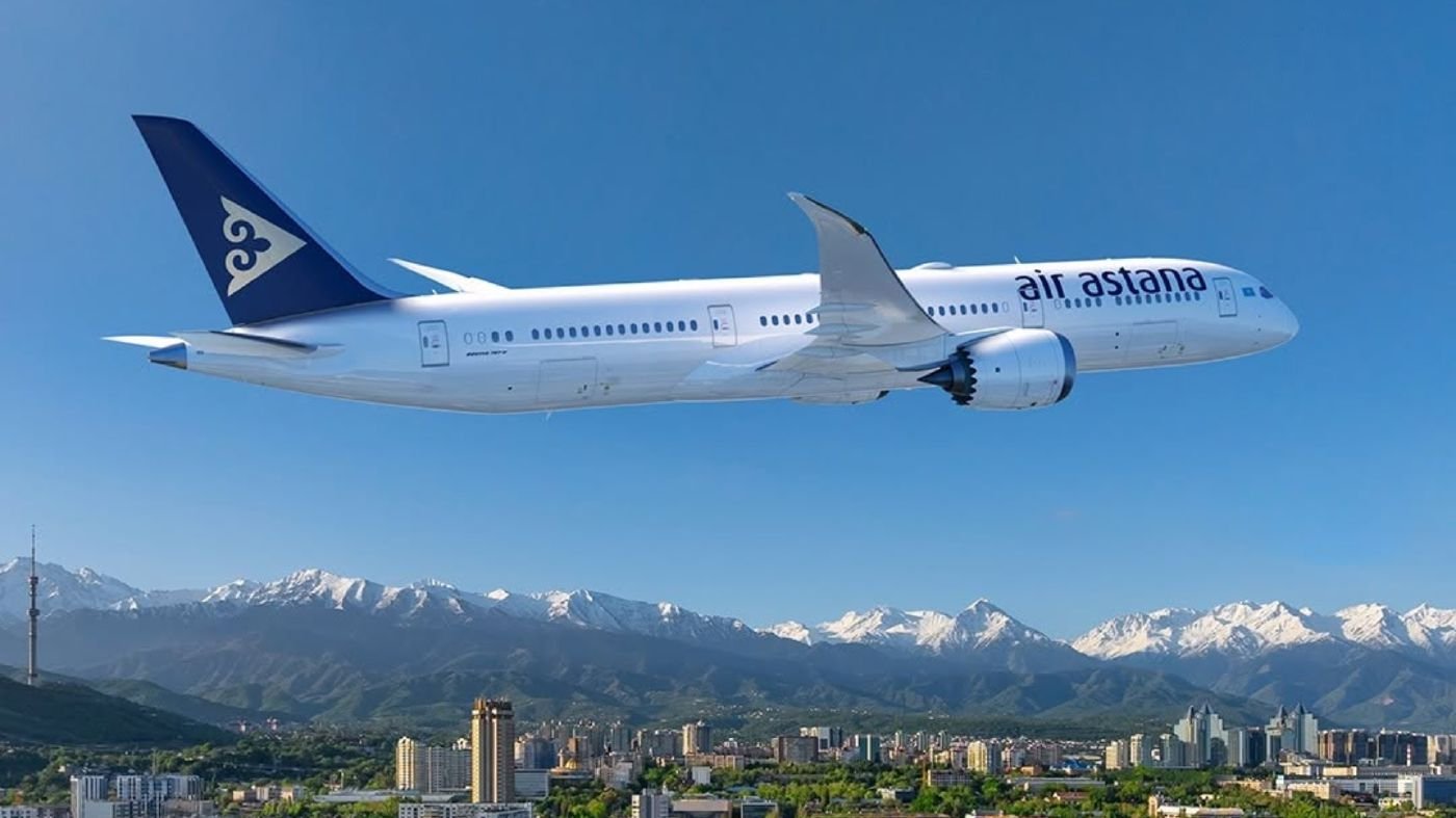 An Air Astana Boeing 787 in flight, with Almaty's skyline and the Tian Shan mountains behind it