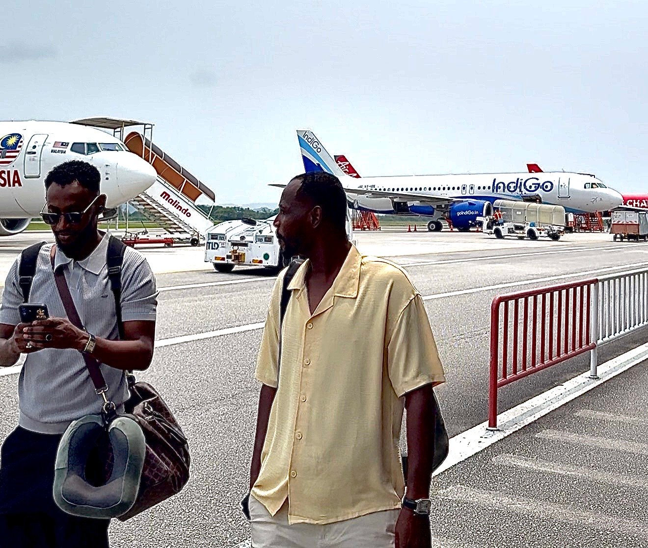Passengers walking across the tarmac at Langkawi International Airport, with a Malindo (Batik Air Malaysia) Boeing 737 and an IndiGo Airbus A320 parked behind them and an AirAsia aircraft at the edge of the frame