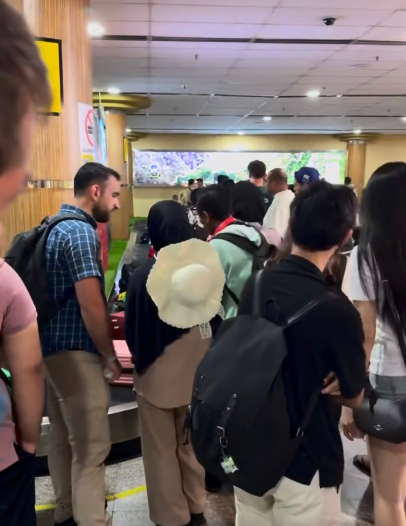 A crowded baggage claim area with arriving passengers and luggage trolleys at Langkawi International Airport