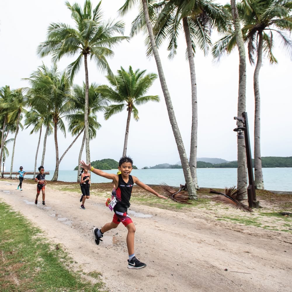 A child running along the beach under palms during an IRONKIDS event (3 of 3)