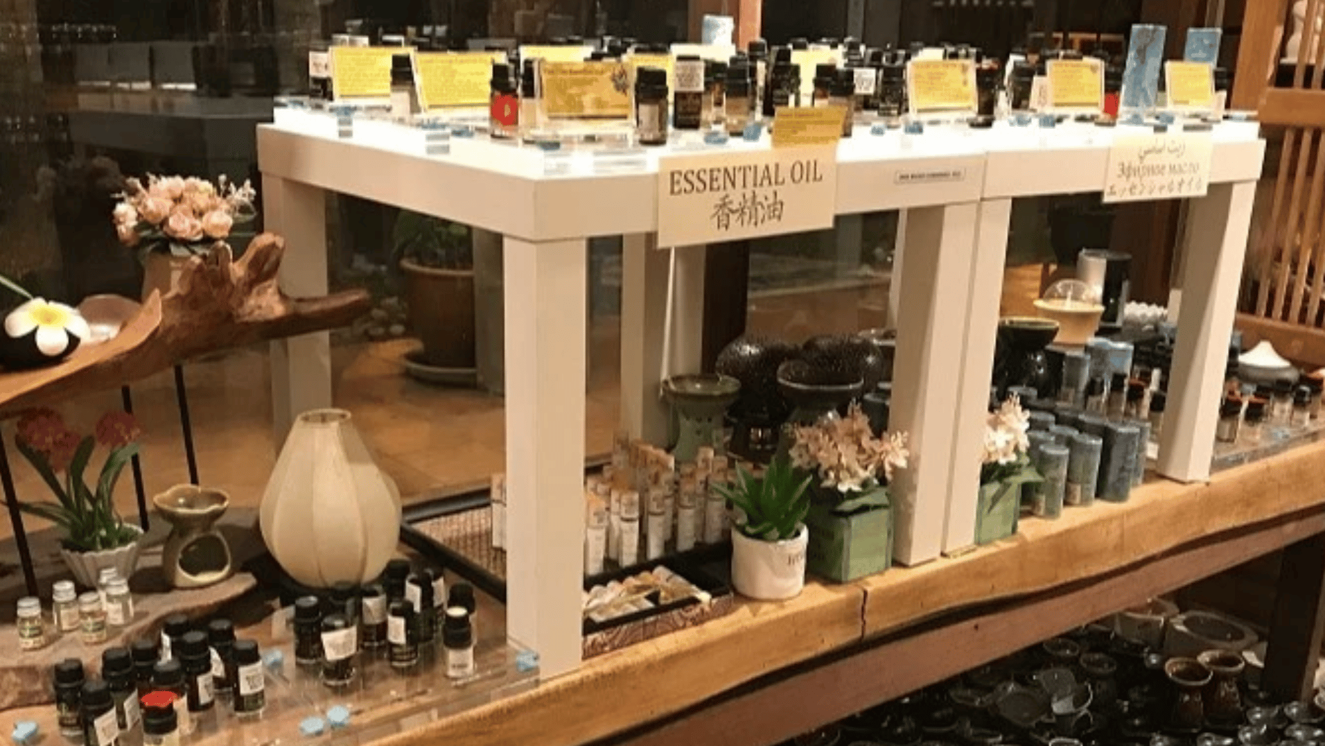 A shop display of essential oil bottles with multilingual signage reading 'Essential Oil', surrounded by burners, candles and aromatherapy products