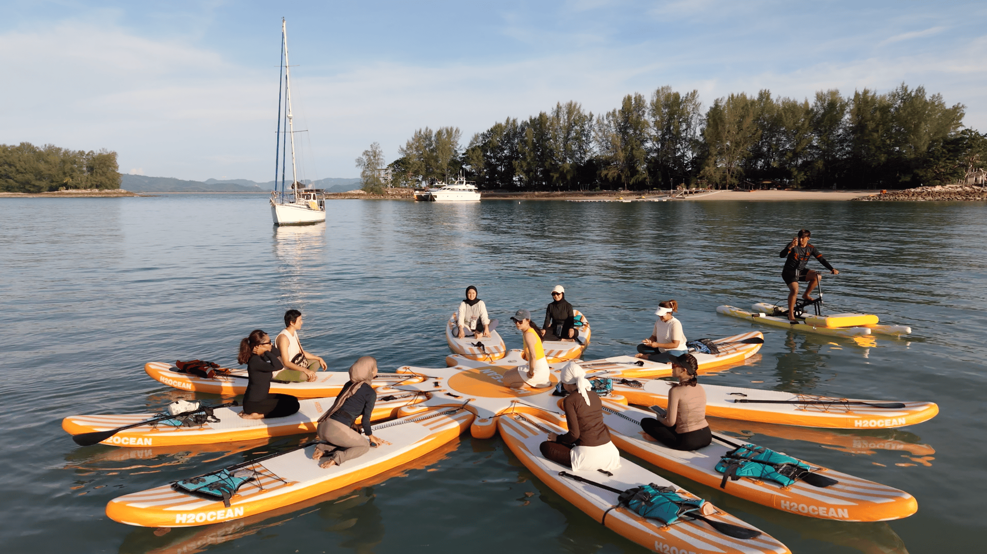 A group doing yoga on a floating paddleboard platform in a sheltered Langkawi bay