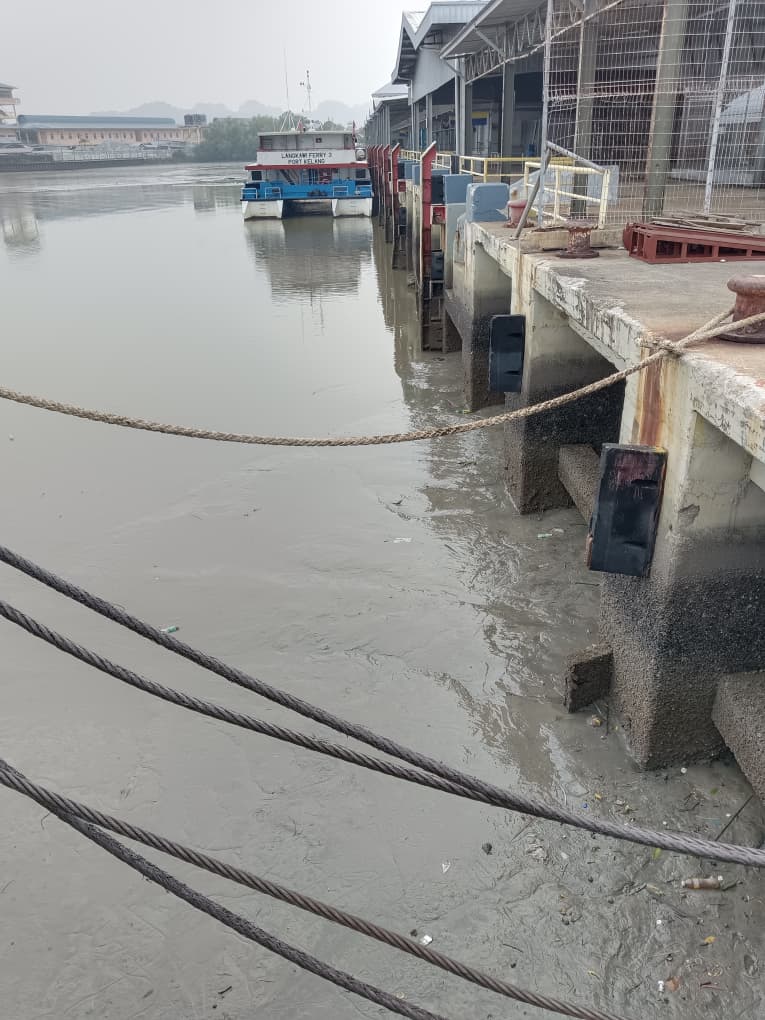 Low tide silting at the Kuala Perlis jetty, with mooring ropes and a ferry vessel visible