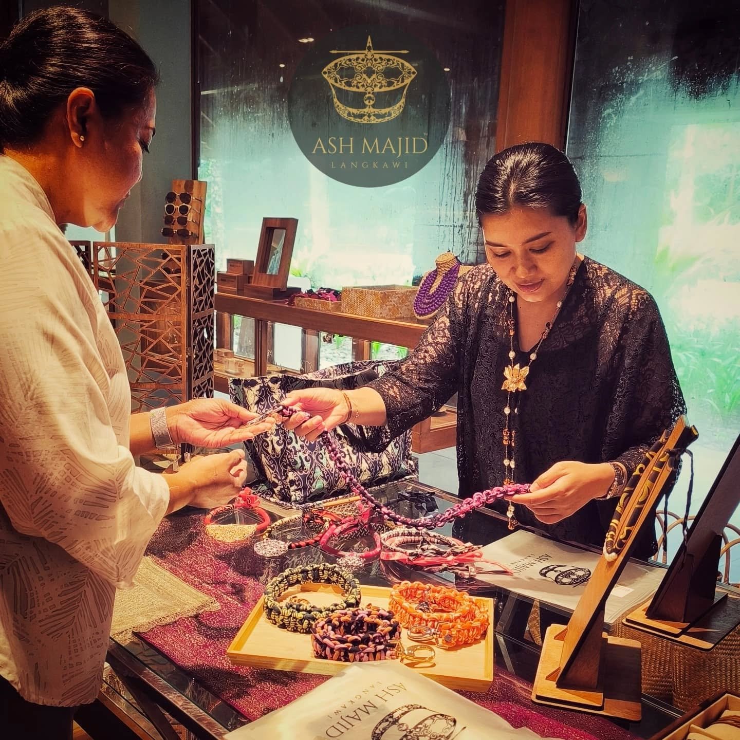 A customer and a shop assistant examining a beaded necklace at Ash Majid Langkawi, a boutique displaying batik-patterned textiles and handmade jewellery