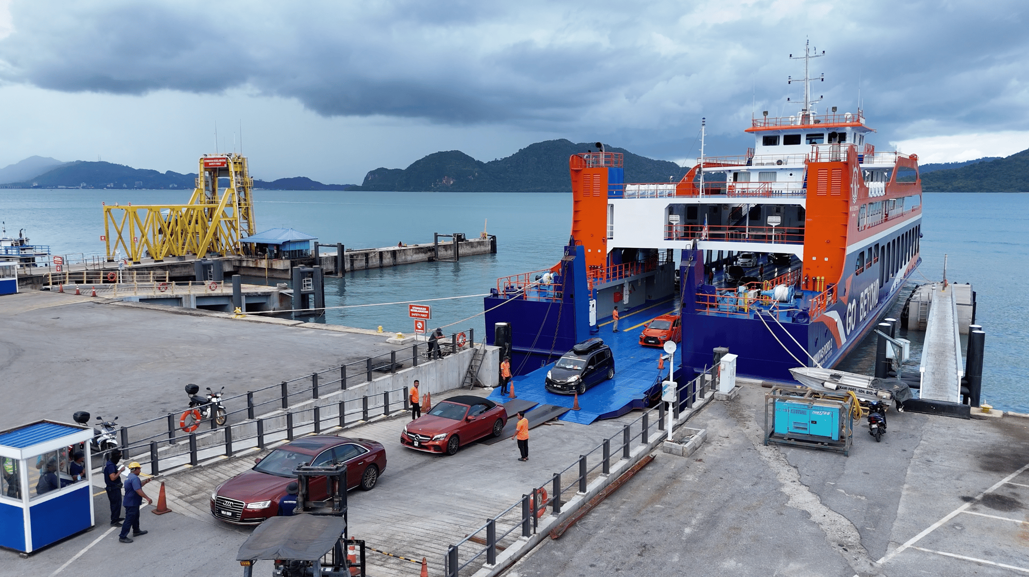A RORO vehicle ferry loading cars at a Langkawi jetty, with hills in the background