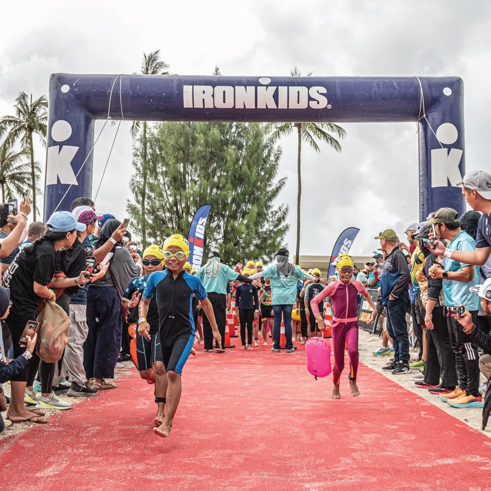 Children in swim caps and goggles wading out of the sea at the start of the run leg of an IRONKIDS aquathlon