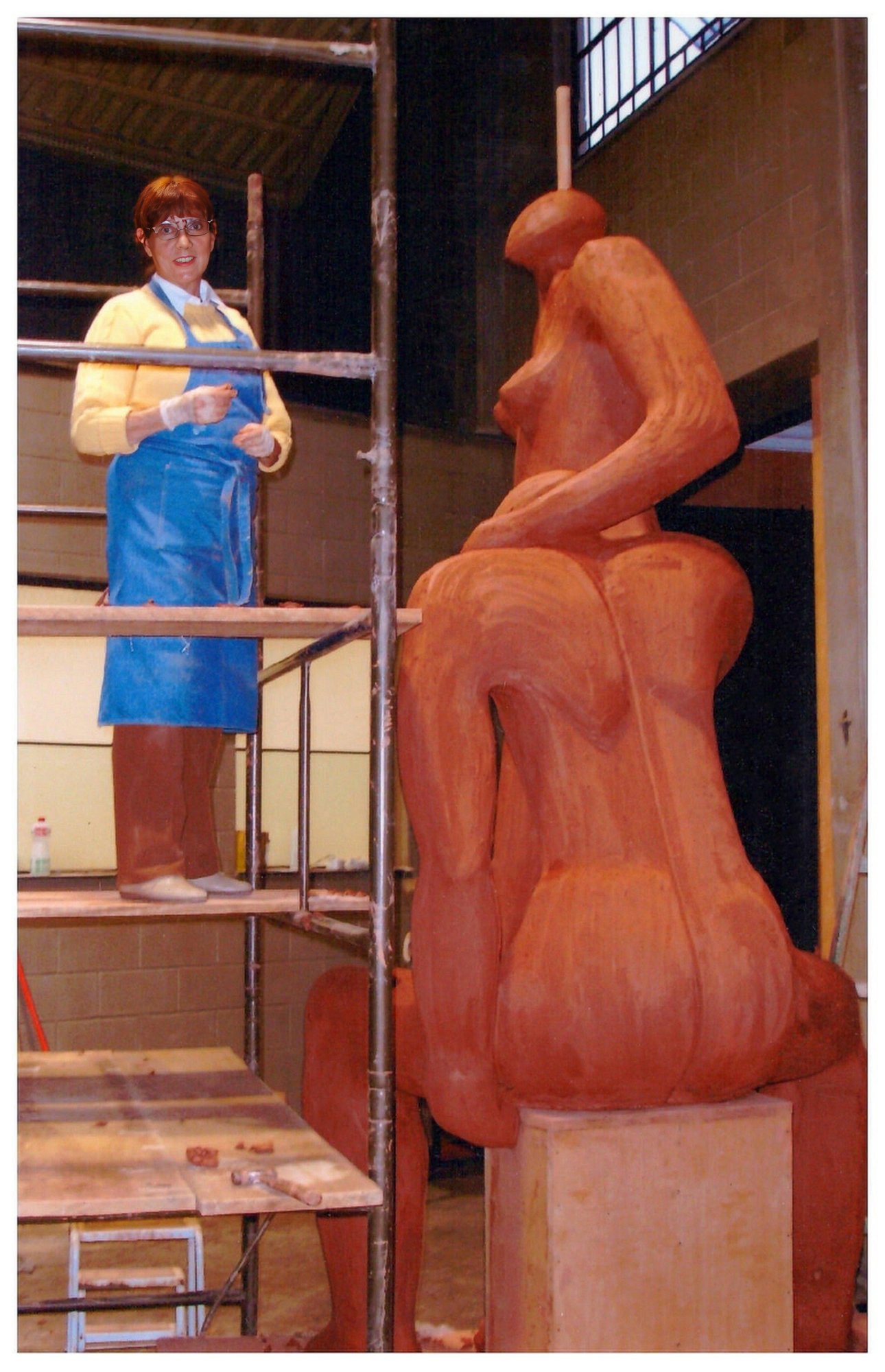 Margarita de avental azul em andaimes criando grande escultura abstrata