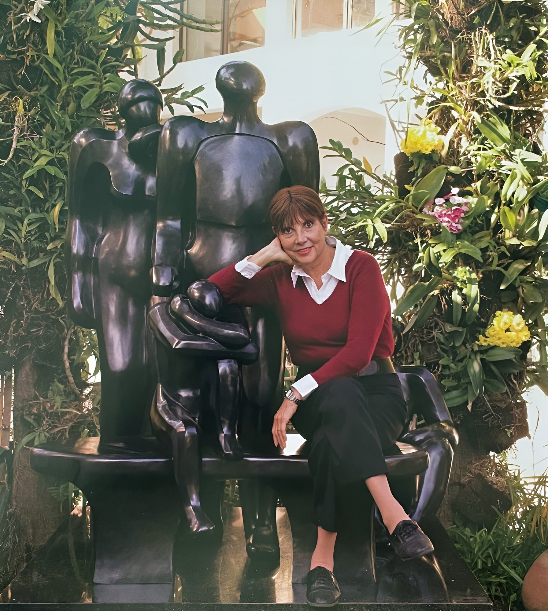 Margarita sentada ao lado de sua escultura de bronze em jardim