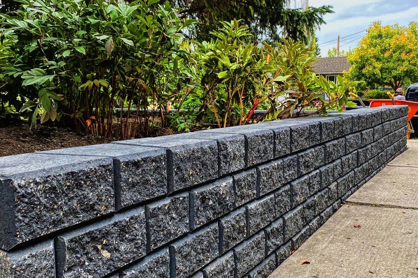 Dark granite block retaining wall with lush shrubs framing a Calgary garden bed, All The Moore Landscaping